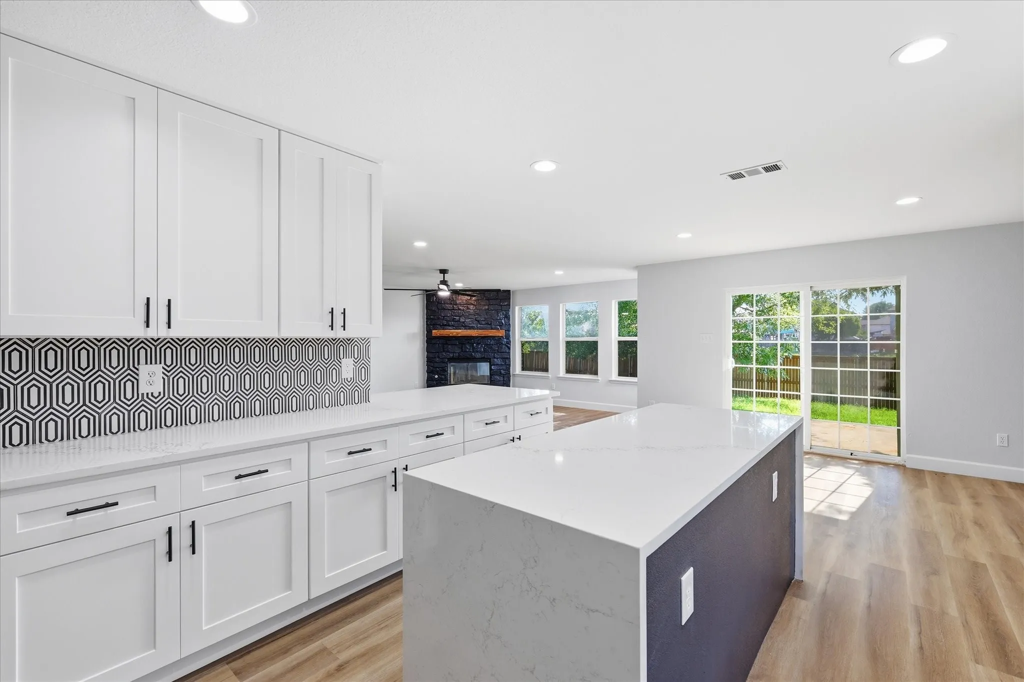 White shaker-style cabinetry with black hardware, geometric tile backsplash, and light-toned countertops