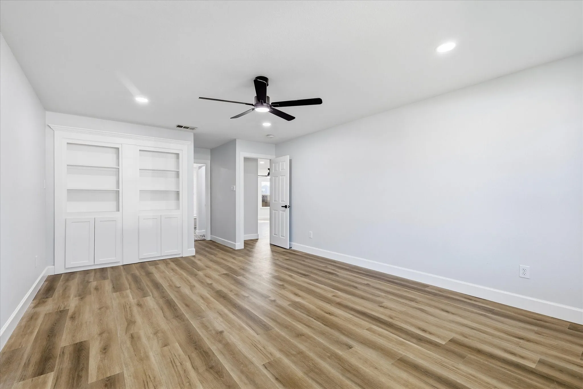 Wood-finish flooring, built-in shelving with lower cabinetry, recessed lighting, and a ceiling fan