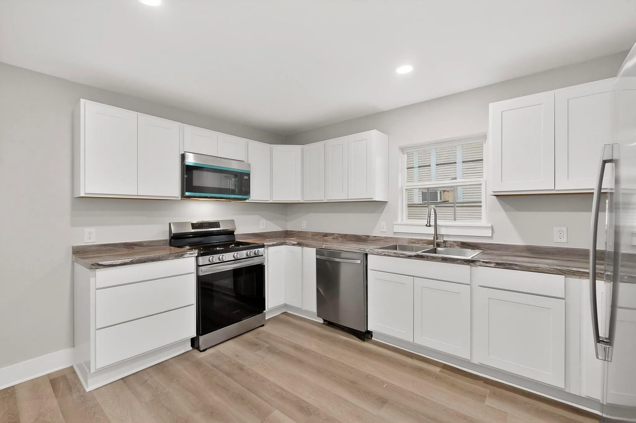 Kitchen featuring white shaker cabinetry, stainless steel appliances, wood-finish flooring, and recessed lighting