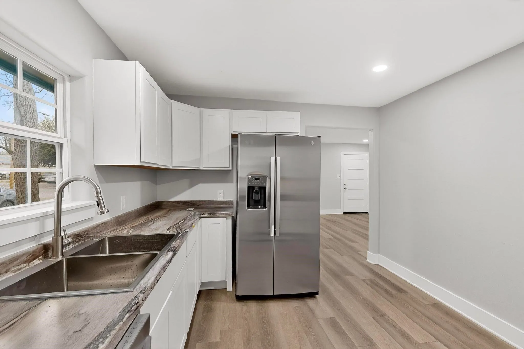 Kitchen featuring wood-finish flooring, white cabinetry, a stainless steel double-basin sink, and a stainless steel side-by-side refrigerator