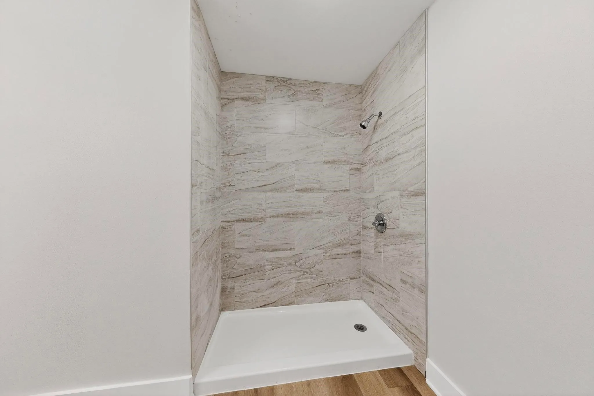 Tiled shower enclosure featuring a white shower pan and a chrome shower head with matching controls