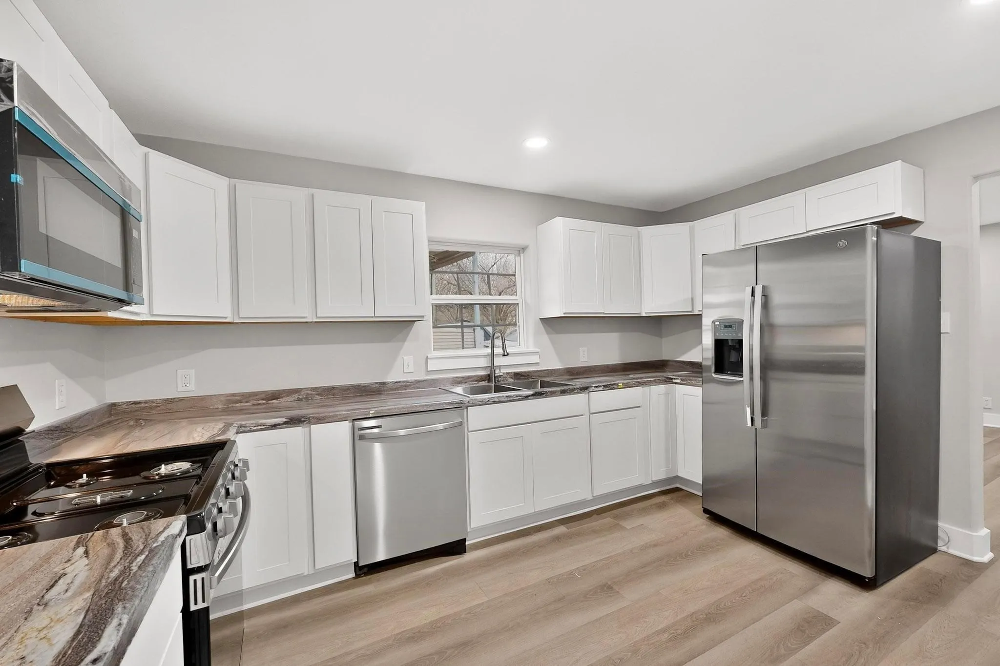 Kitchen featuring white cabinetry, wood-finish flooring, stainless steel appliances, a double basin sink, and ample countertop space