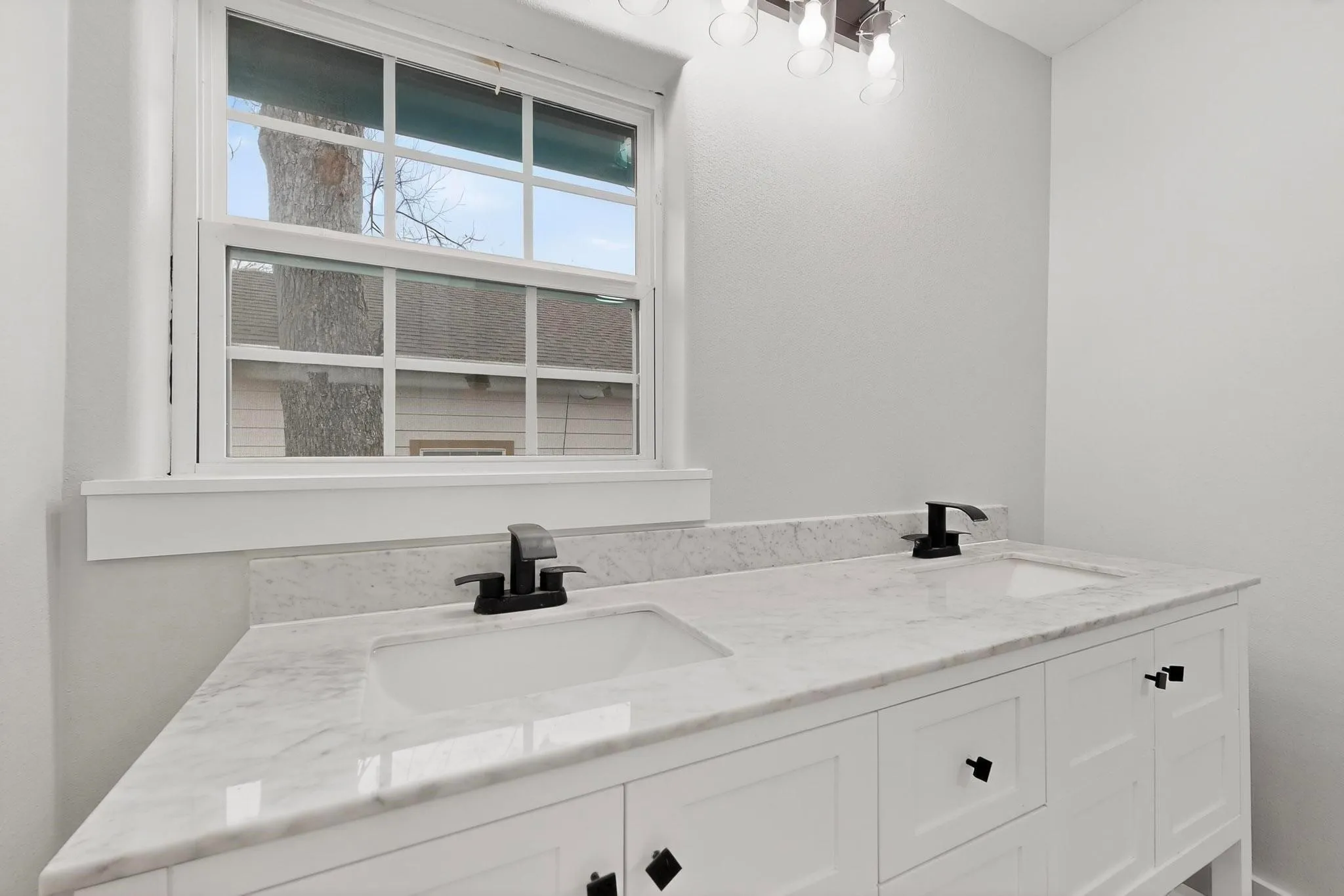 Dual basin vanity with white cabinetry, square black hardware, and light-toned countertops
