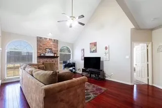 Living area with dark wood-flooring, high vaulted ceiling, ceiling fan, and a brick fireplace