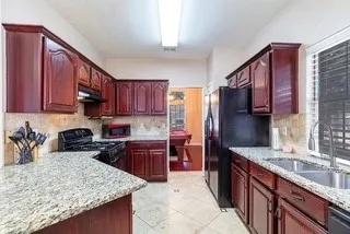 Kitchen with black appliances, brown cabinets, and light granite counters