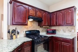 Kitchen with black range with gas stovetop, under cabinet range hood, decorative backsplash, and granite countertops