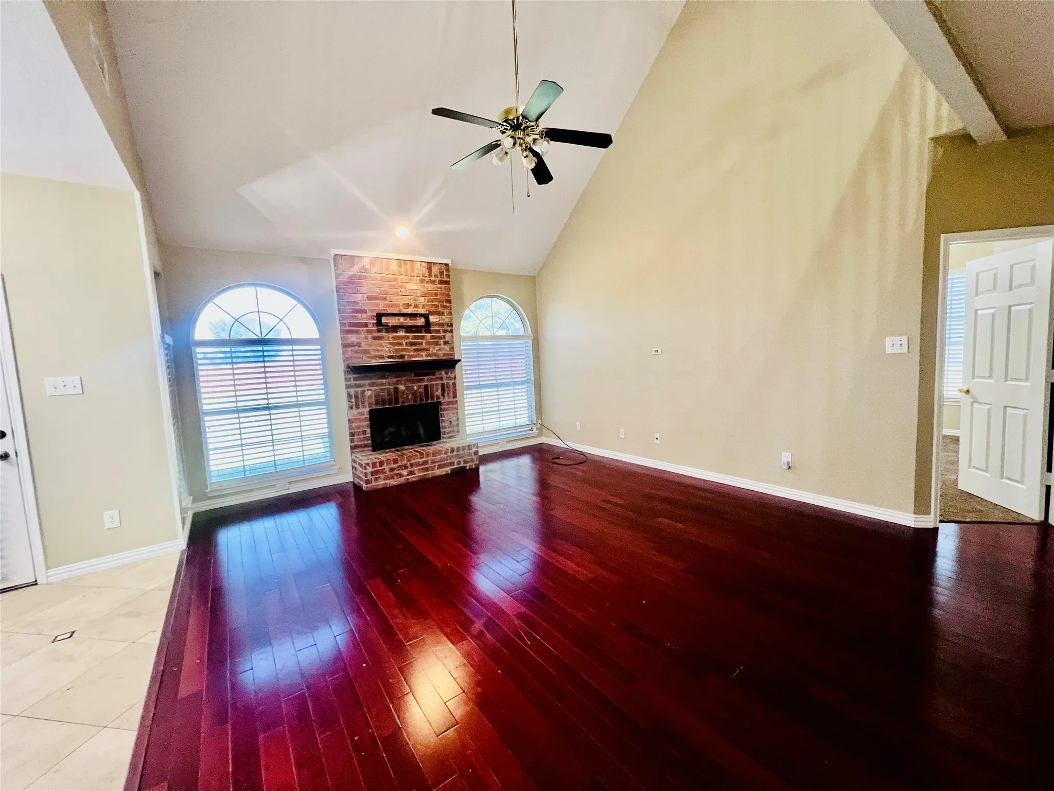 Unfurnished living room featuring a ceiling fan, a brick fireplace, light wood-type flooring, and high vaulted ceiling