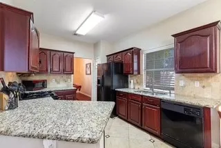 Kitchen with decorative backsplash, dishwasher, a peninsula, light tile patterned floors, and light stone counters