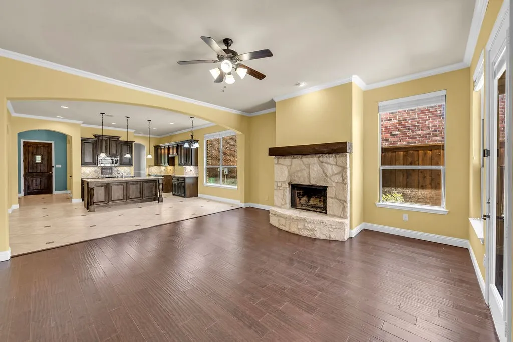 Wood-finish flooring, stone-clad fireplace with wood mantle, overhead ceiling fan, arched entryway, and tile flooring in the kitchen