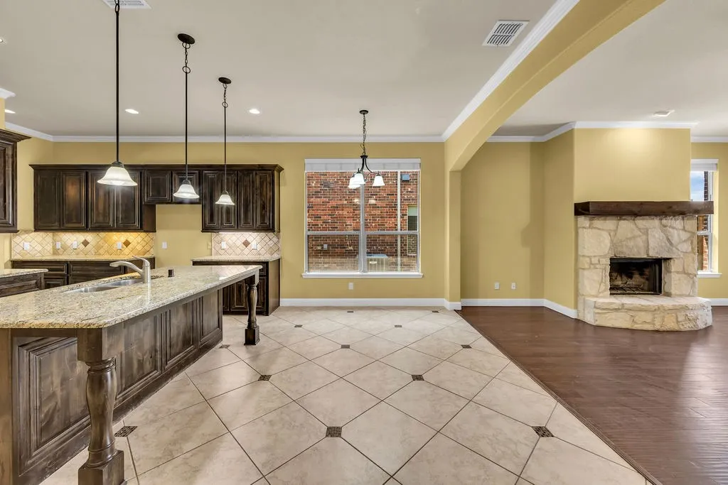 Kitchen island with an undermount sink, dark wood-finish cabinetry, light-toned stone countertops, and pendant lighting