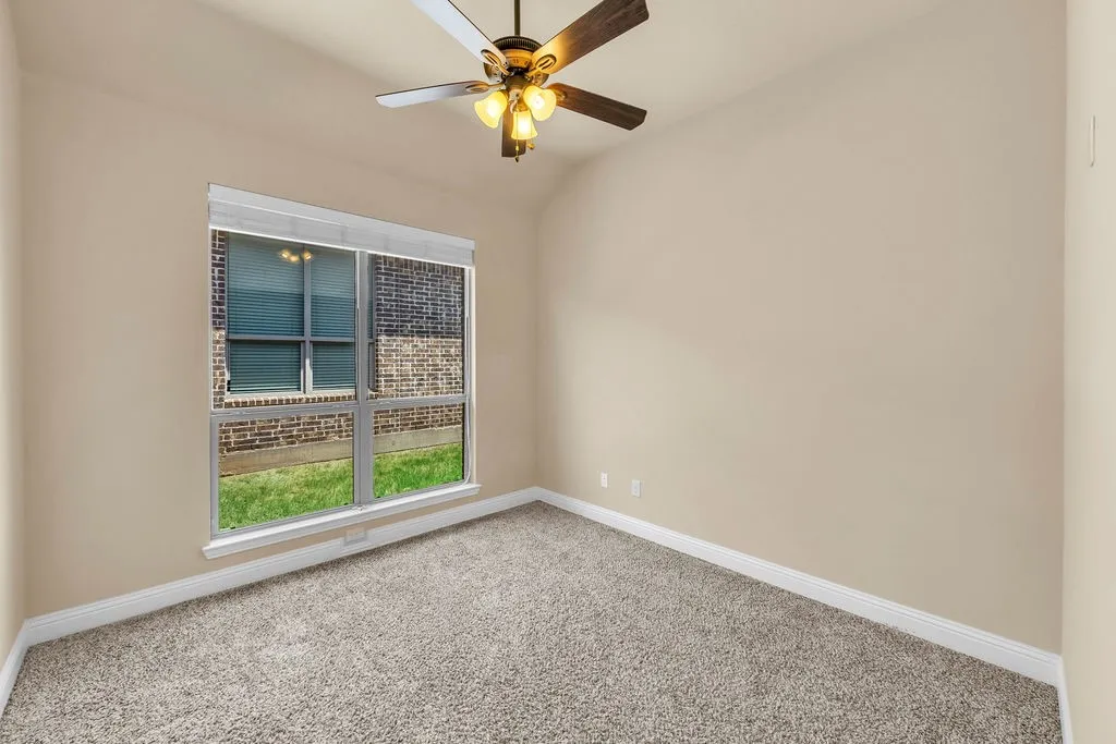 Neutral wall paint, plush carpet flooring, ceiling fan with light fixture, large window with blinds, and white trim