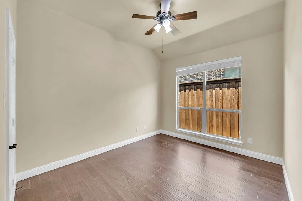 Vaulted ceiling with an attached ceiling fan, wood-finish flooring, and a large window