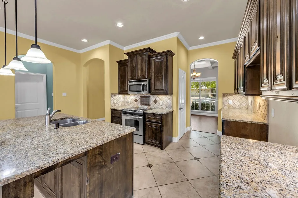 Kitchen featuring granite countertops, wood-finish cabinetry, stainless steel appliances, tile flooring, and pendant lighting