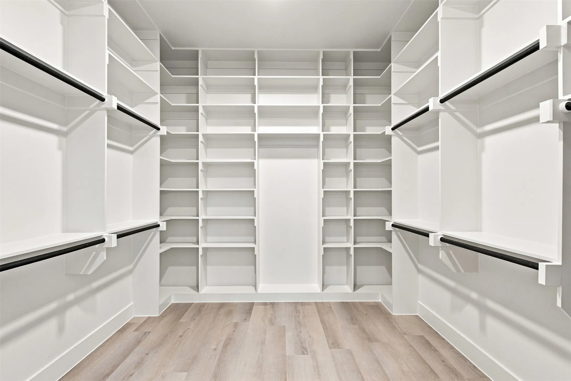 Built-in closet system with extensive shelving, multiple hanging rods, and wood-finish flooring