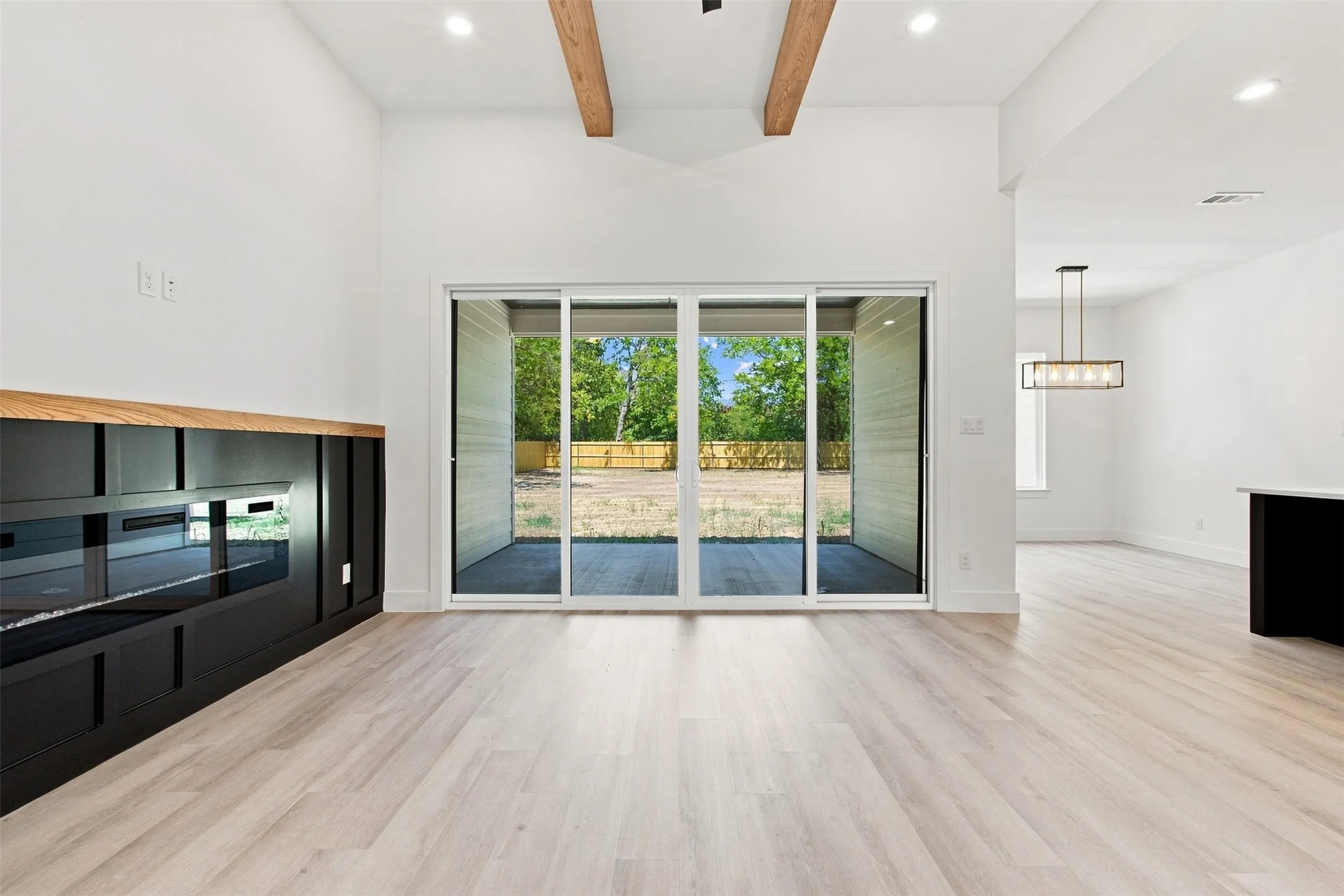 Vaulted ceiling with wood beams, light wood-finish flooring, built-in fireplace feature with wood mantel, recessed lighting, and sliding glass doors to outdoor patio