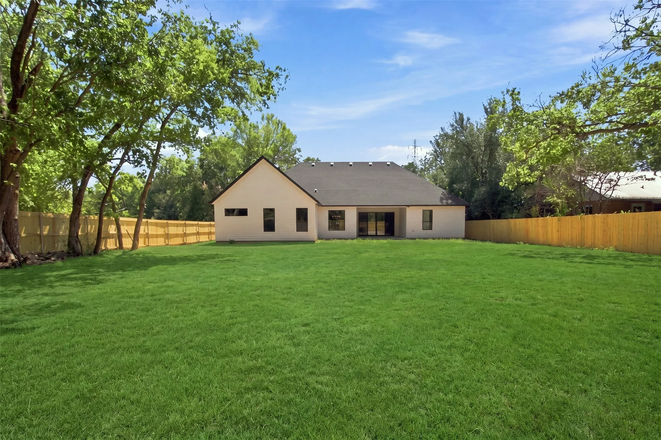 Expansive grassy yard with a wooden privacy fence, mature trees, and a neutral-toned exterior