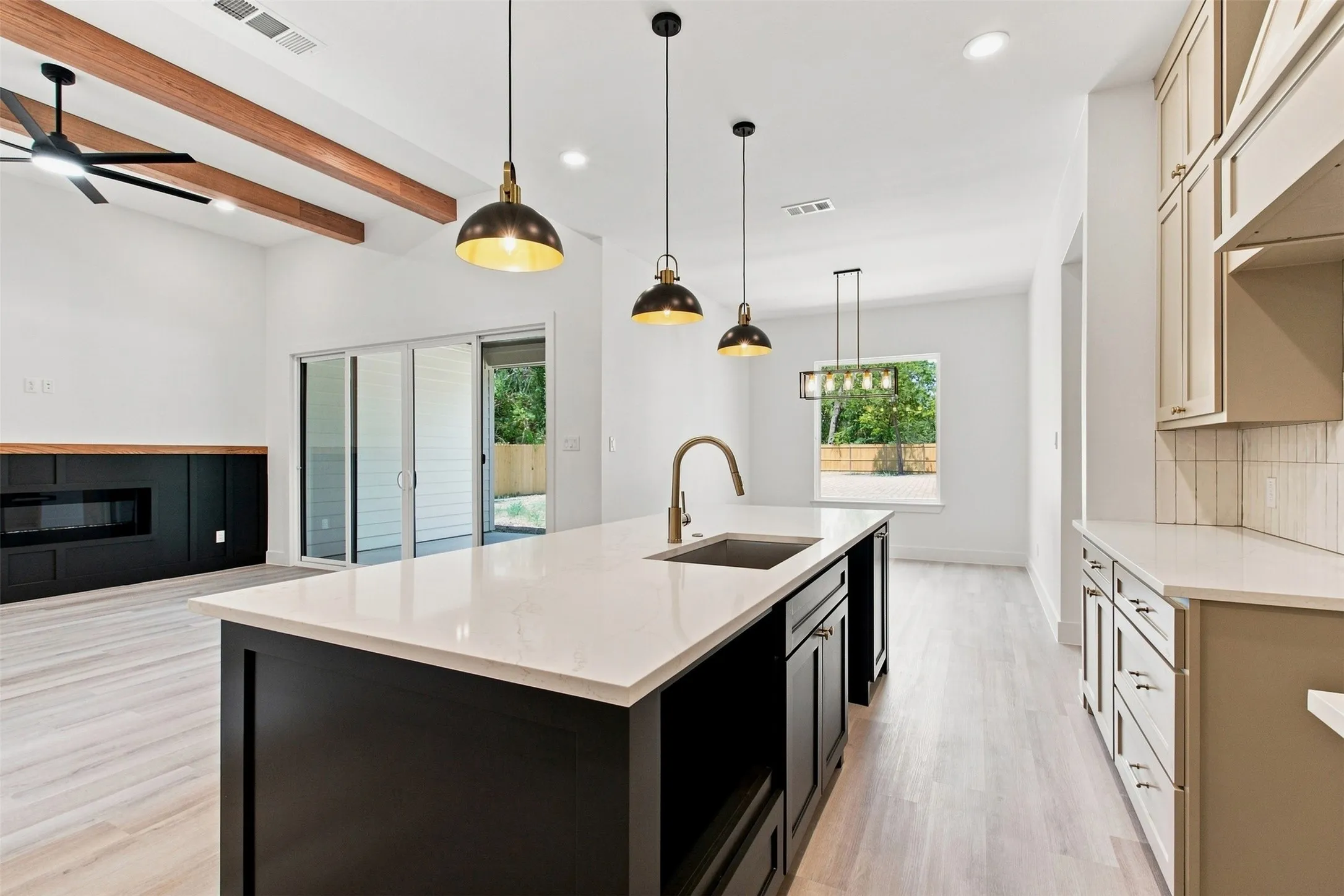 Spacious open-concept interior featuring light wood-finish flooring, a kitchen island with a built-in sink, and ceiling-mounted light fixtures