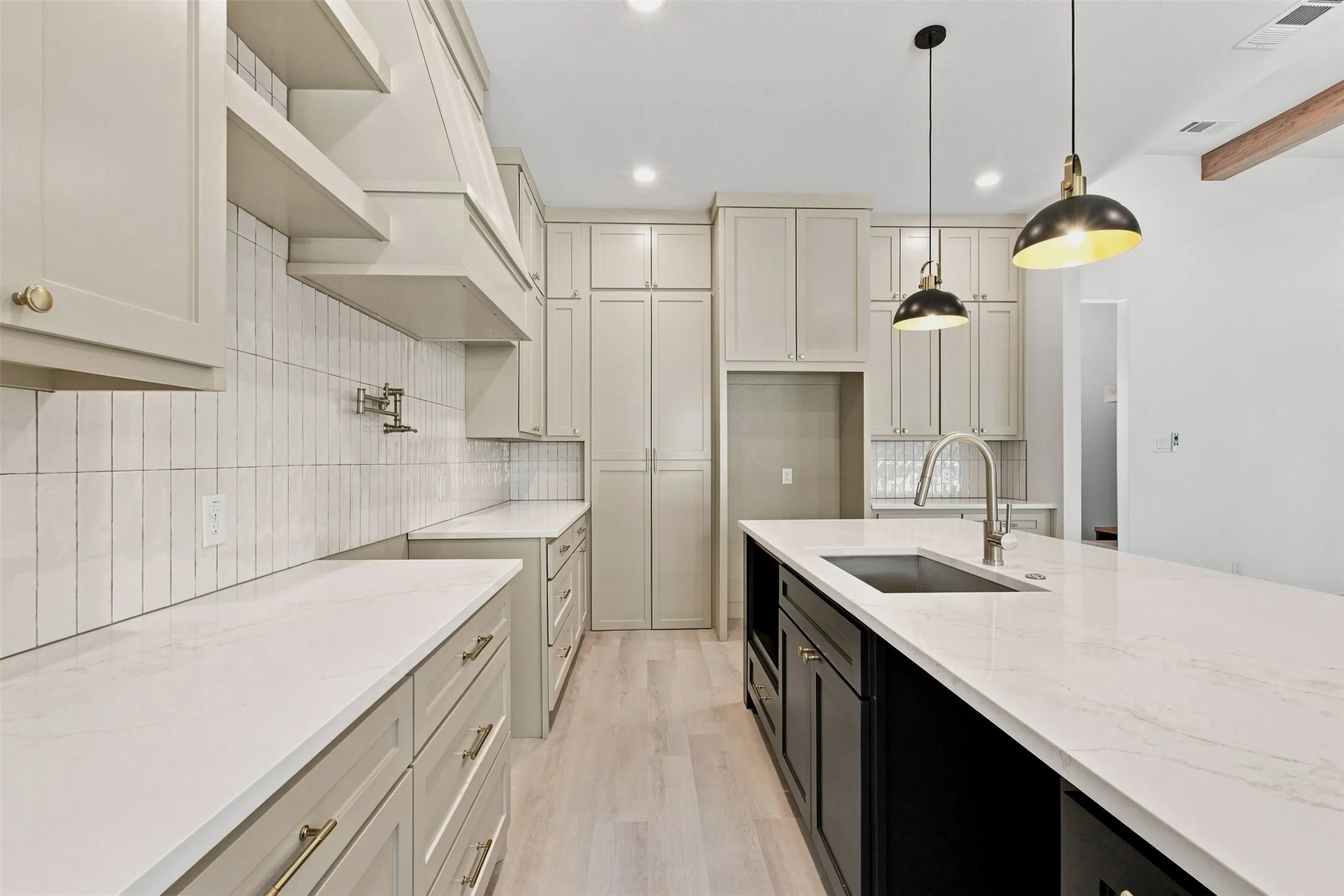 Light-toned cabinetry, vertical tile backsplash, extensive counter space, center island with integrated sink, and pendant lighting
