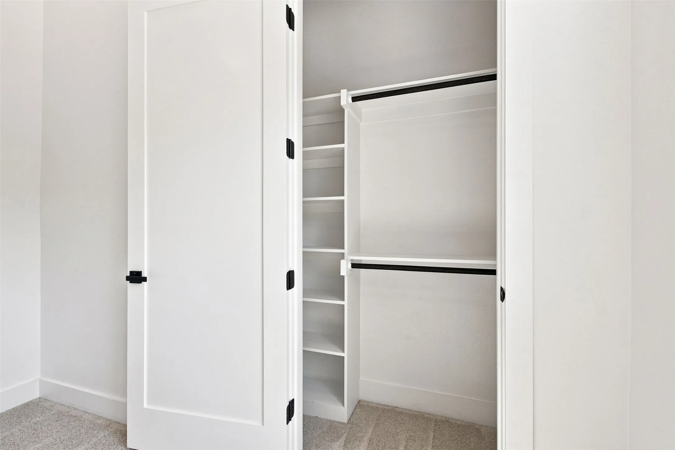 White closet doors with black hardware, built-in shelving, and dual hanging rods