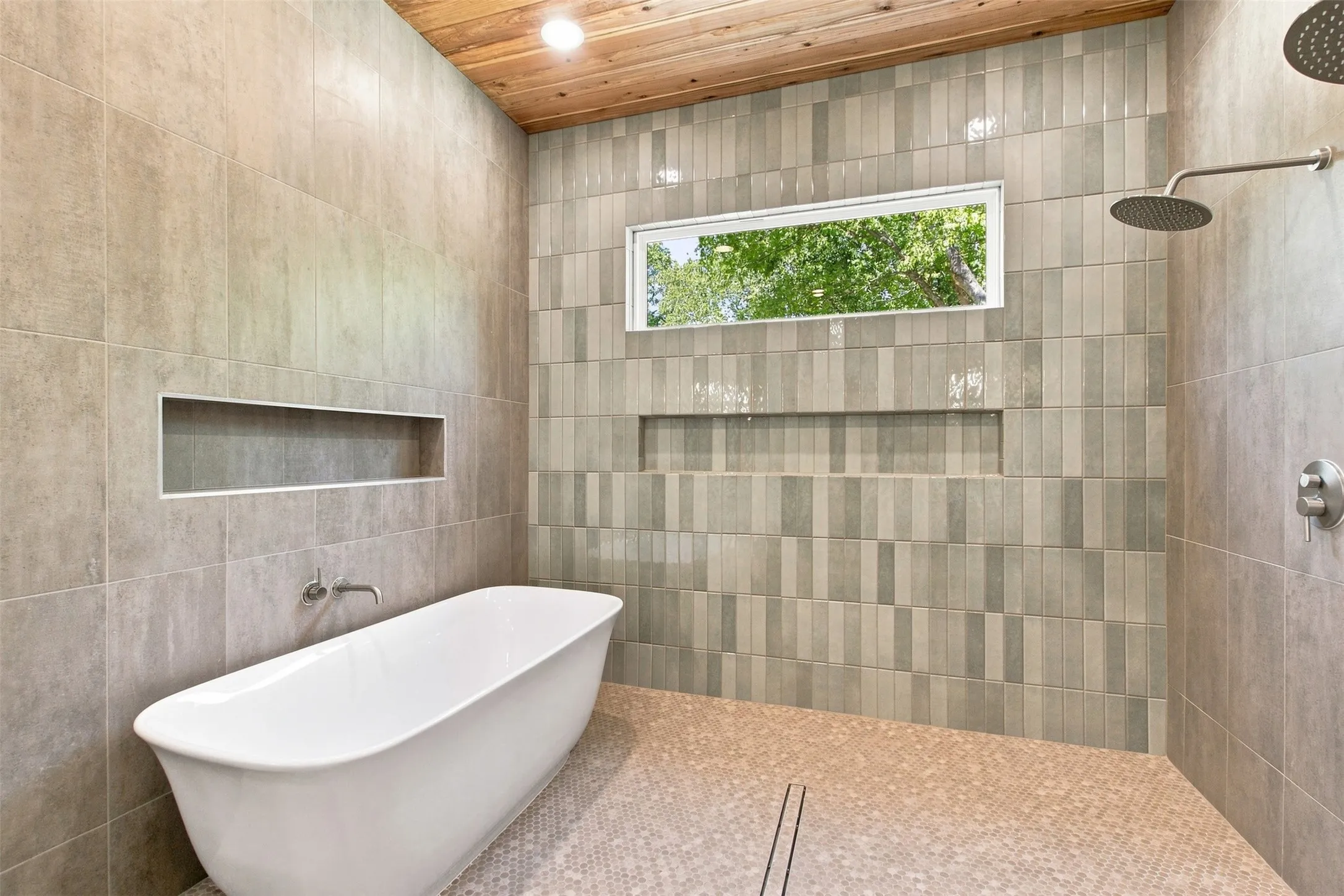 Freestanding soaking tub with a wall-mounted faucet, wood-finish ceiling, tiled shower with a rain shower head, and a built-in shower niche