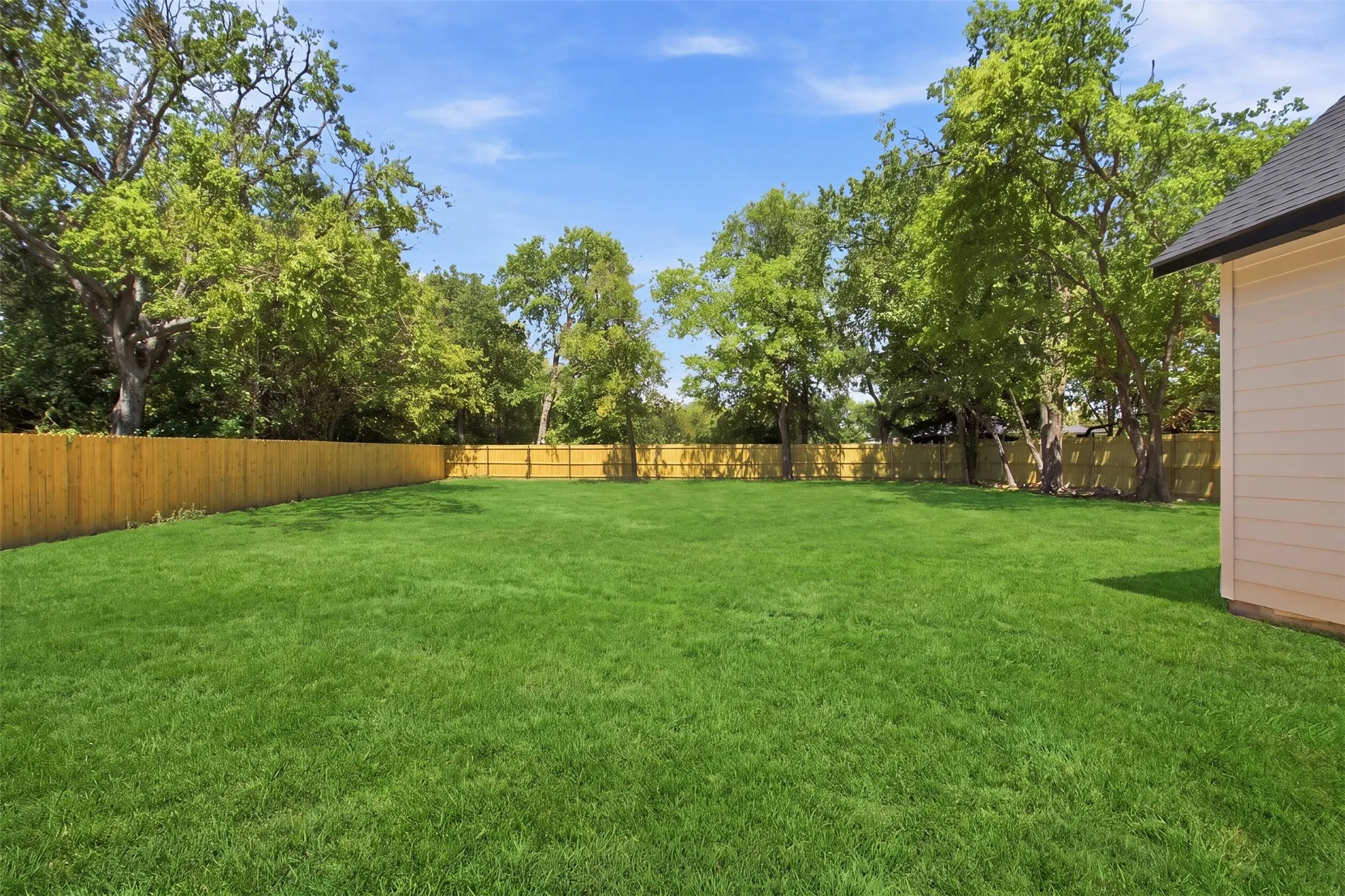 Expansive rear yard featuring a privacy fence and mature perimeter trees