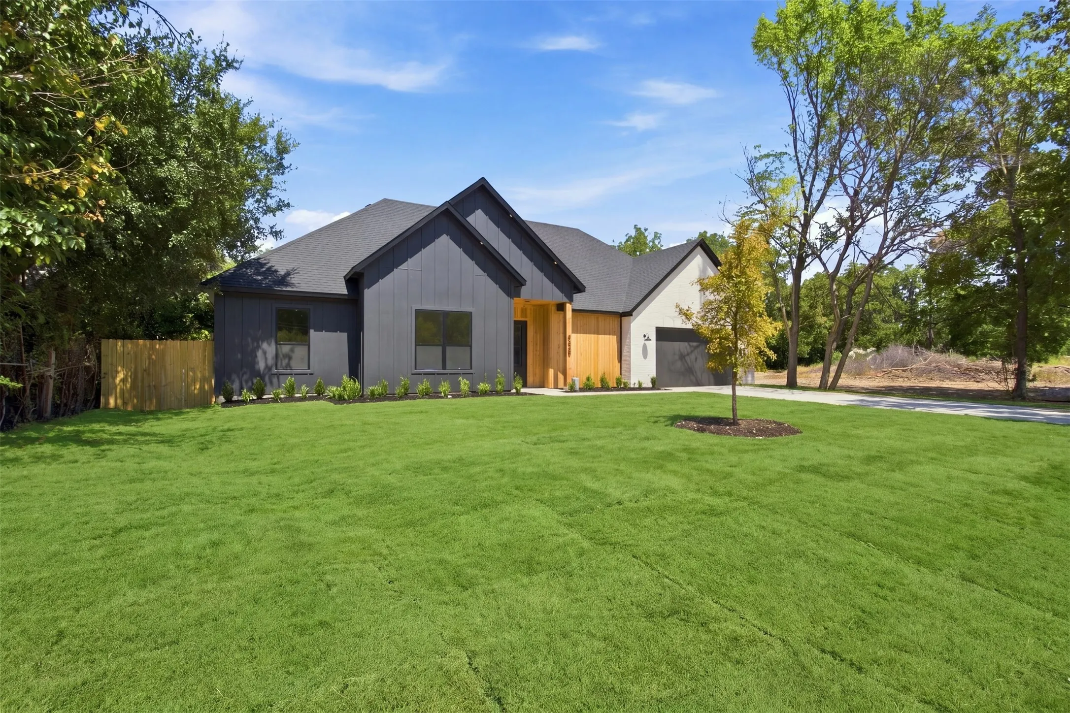 Contemporary exterior with dark siding and wood-finish accents, featuring a dark asphalt shingle roof, a two-car garage, and a lush green lawn
