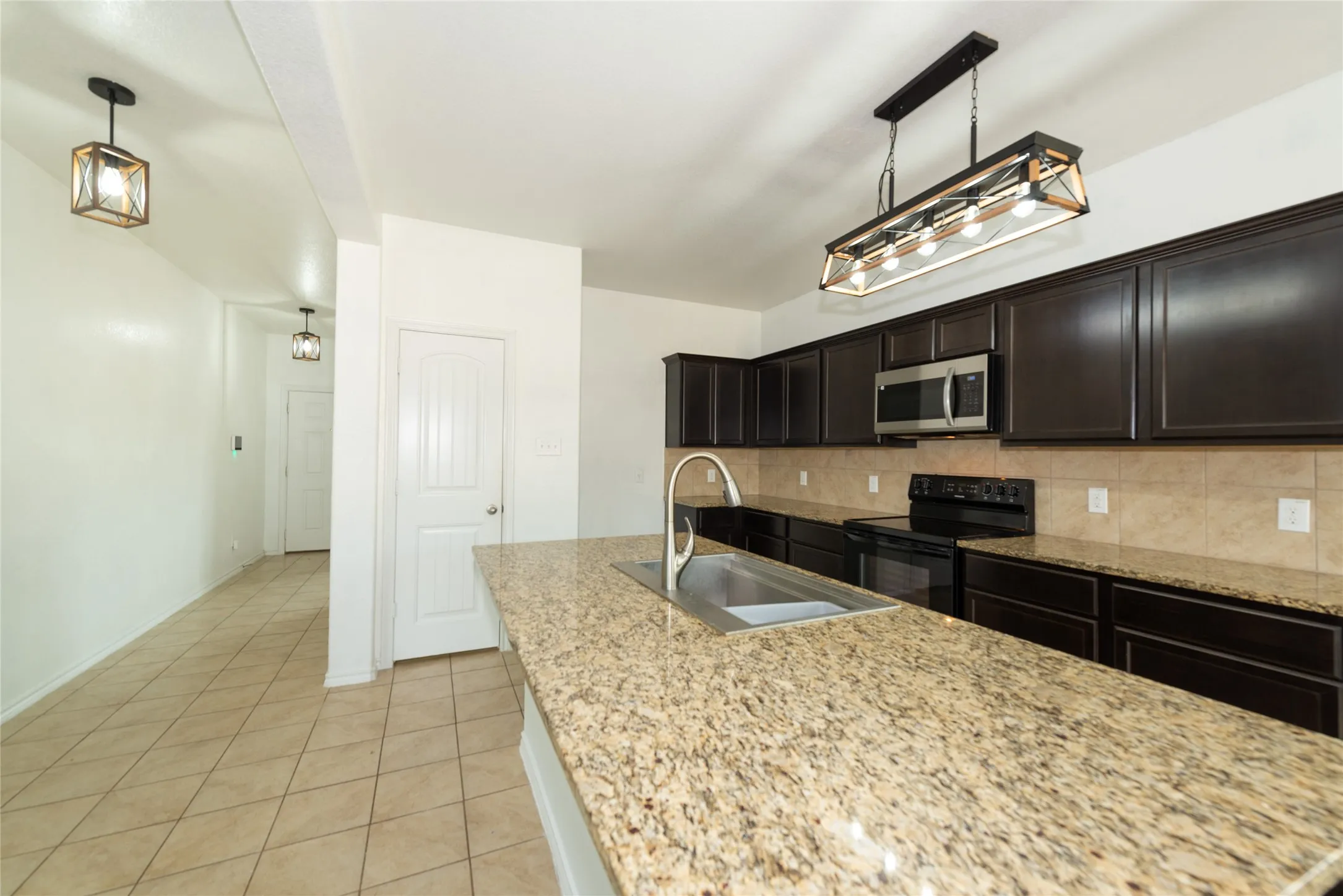 Kitchen featuring dark wood-finish cabinetry, granite countertops, stainless steel microwave, black electric range, and a tile backsplash