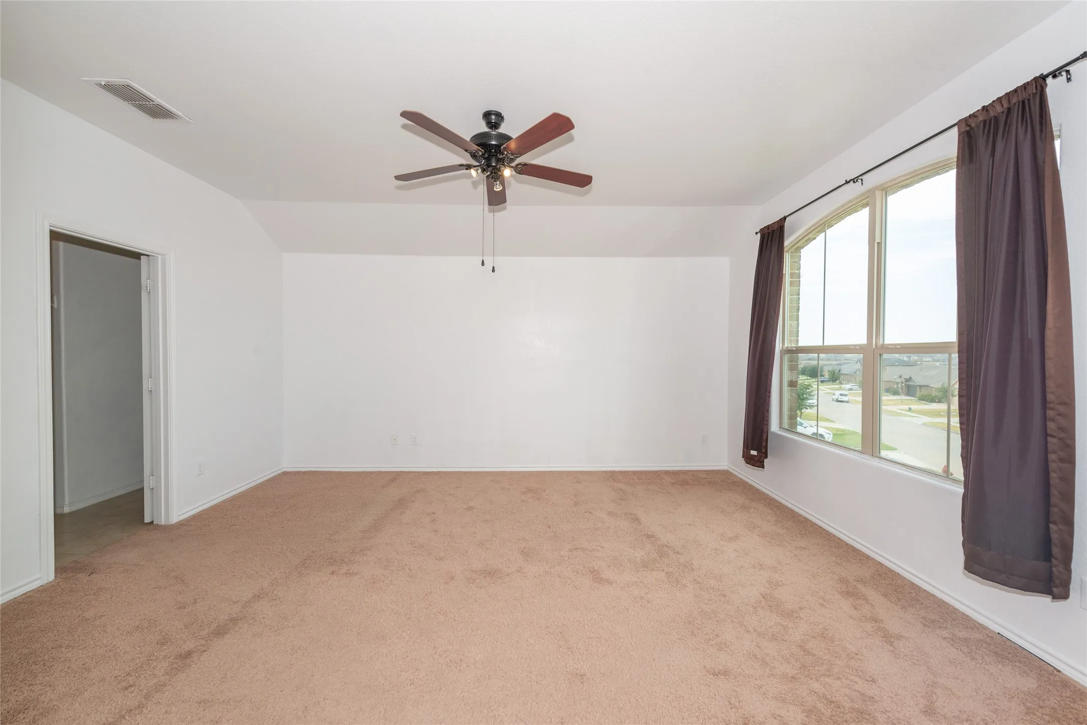 Spacious room featuring vaulted ceilings, a ceiling fan with integrated lighting, and a large arched window
