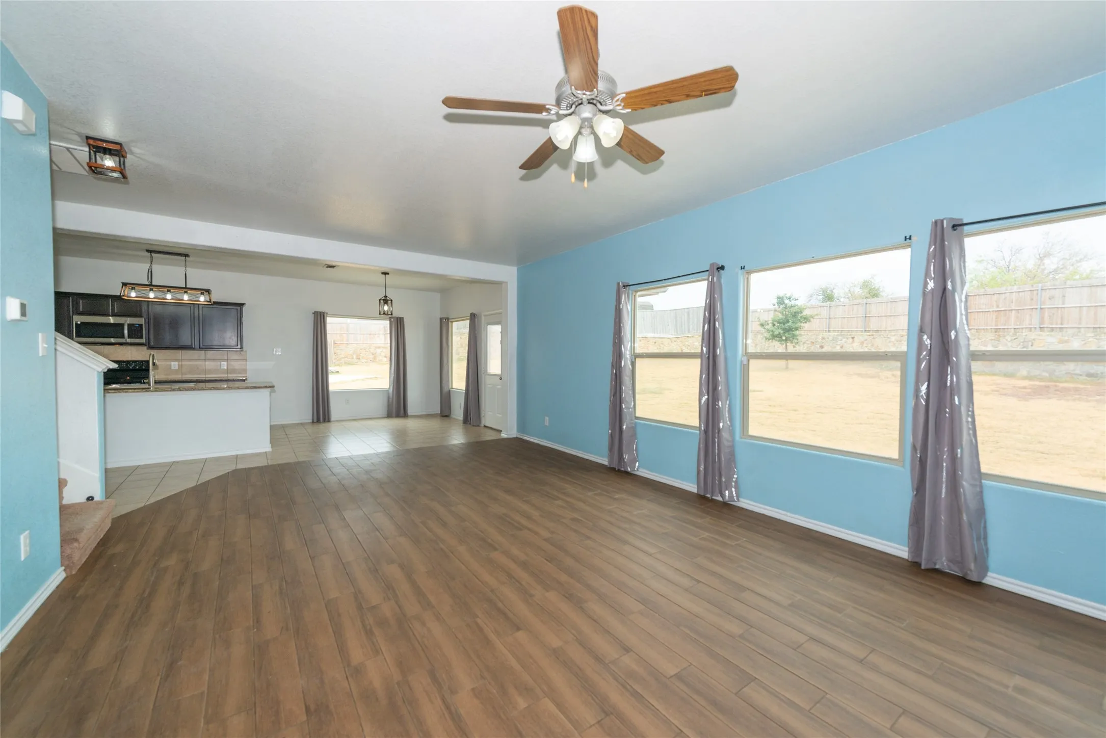 Spacious room featuring wood-finish flooring, a ceiling fan, and multiple windows