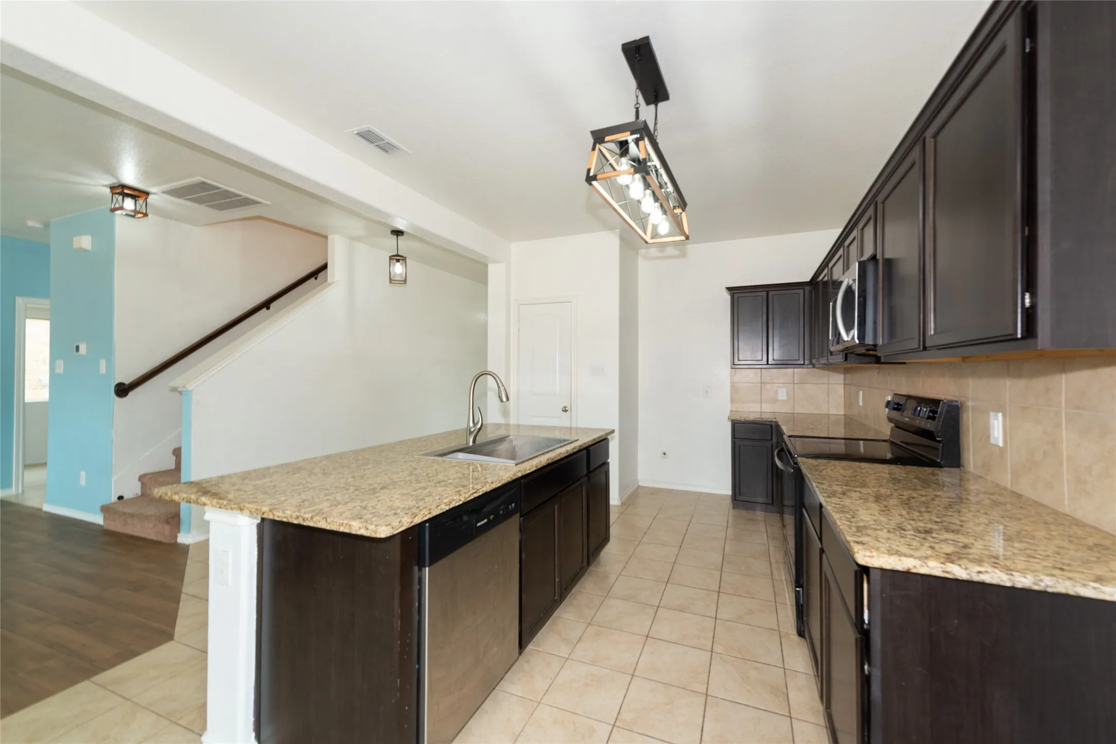 Kitchen featuring a large island with a stainless steel sink, dark wood-finish cabinetry, light-toned tile flooring, and light-toned countertops