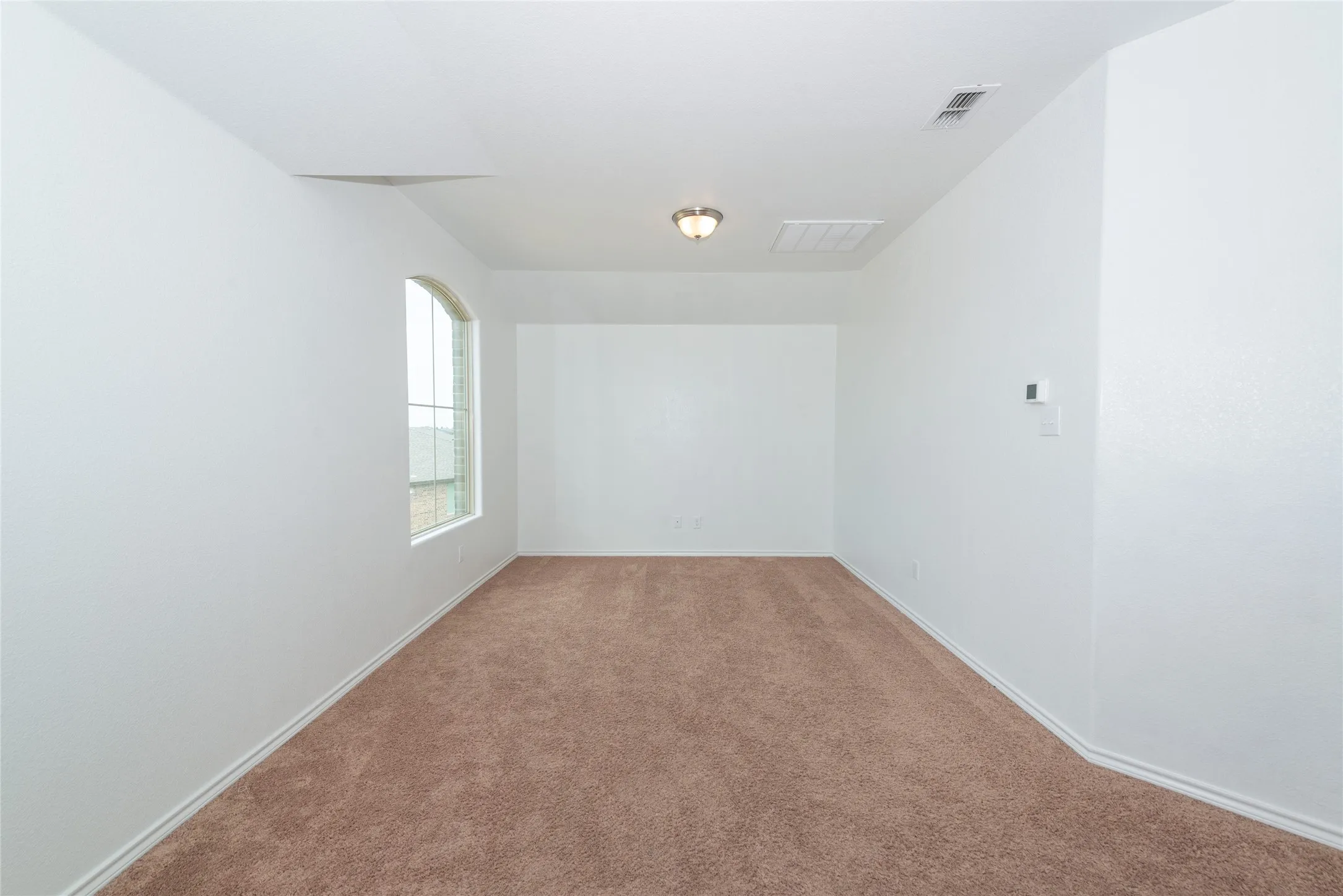 Arched window with gridded panes, brown carpeting, and a flush-mount ceiling light
