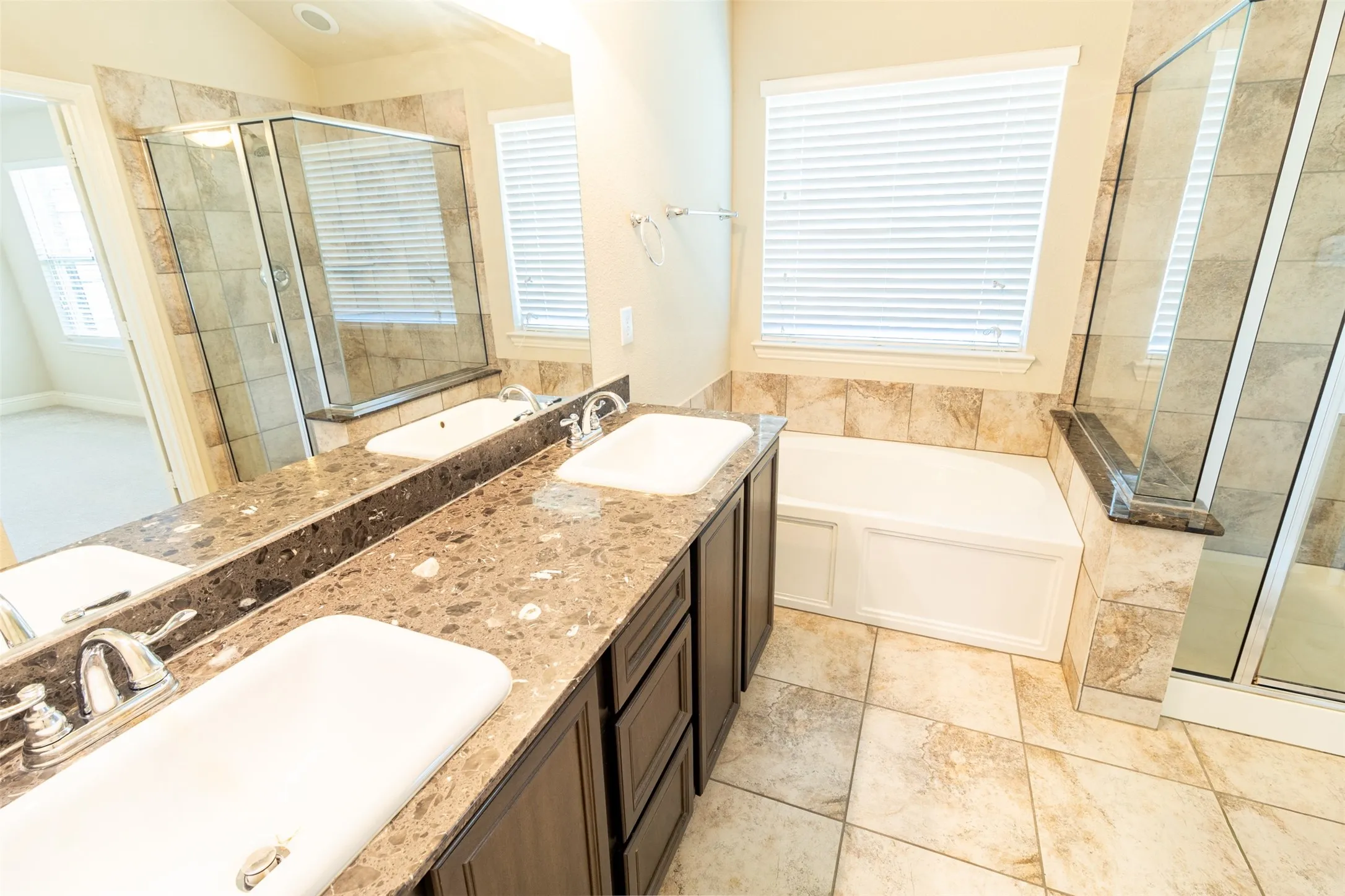 Dual vanity with integrated sinks, spacious corner bathtub, walk-in shower with glass enclosure, and tiled flooring