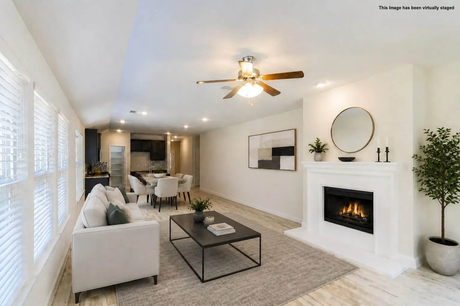 Virtual staged=>Living area with light-toned wood-finish flooring, a white mantel fireplace, and a ceiling fan