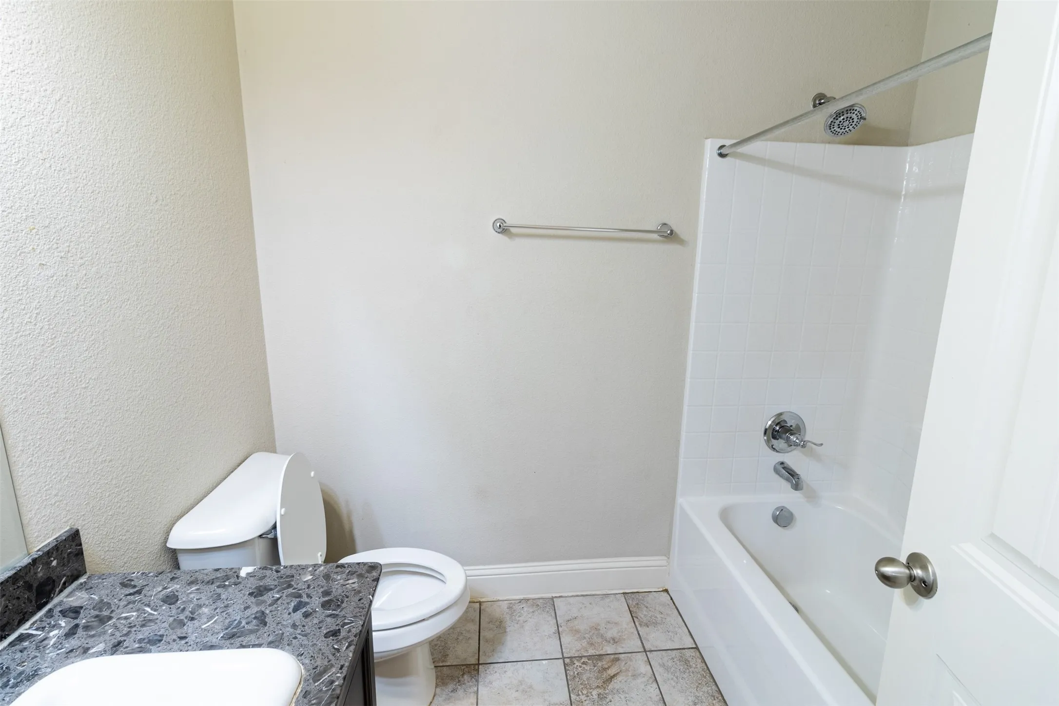 Full bathroom featuring a tub/shower combination with a white subway tile surround, a toilet, and a vanity with a dark countertop and integrated sink