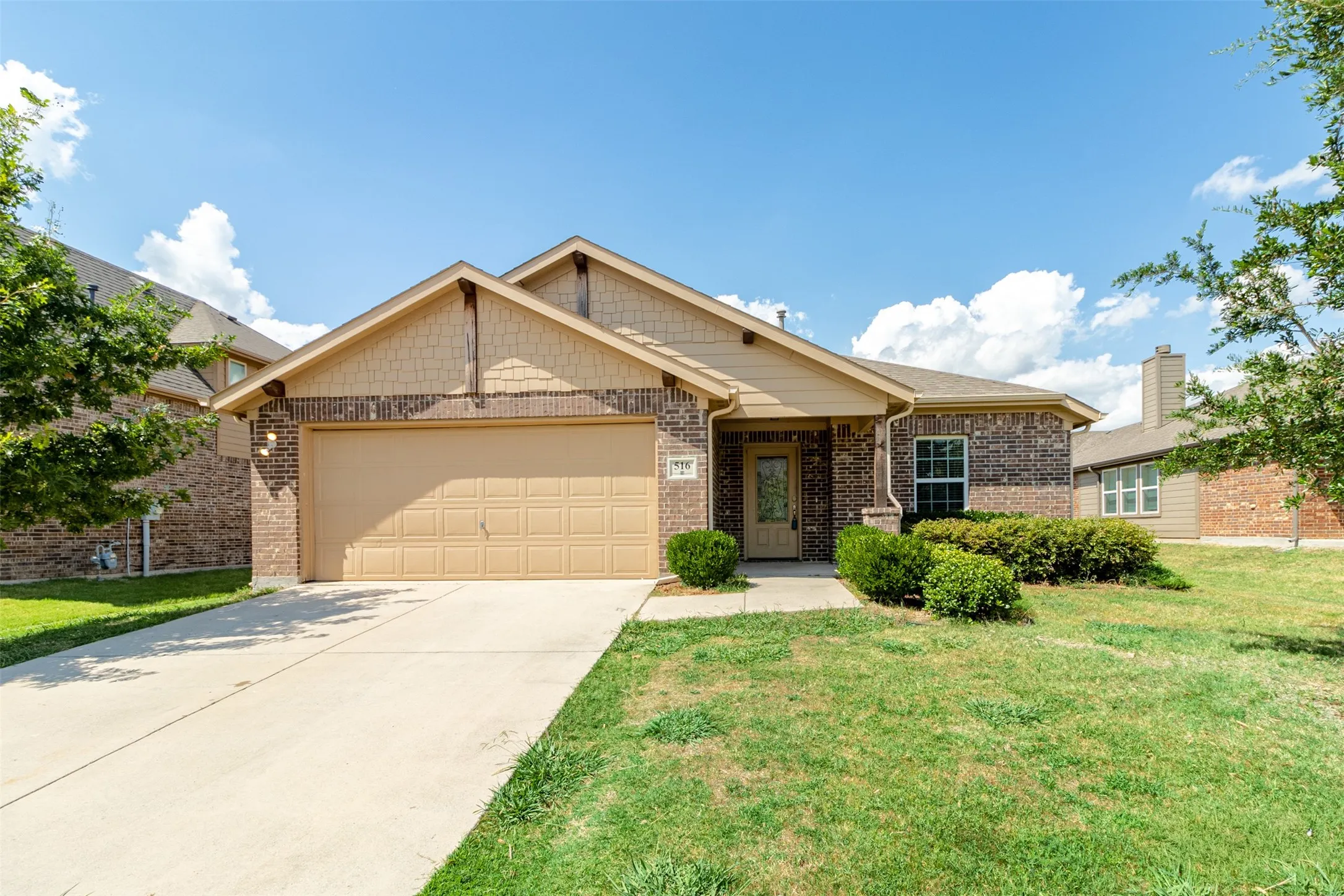 Brick exterior with decorative gables, an attached garage, a concrete driveway, and established landscaping
