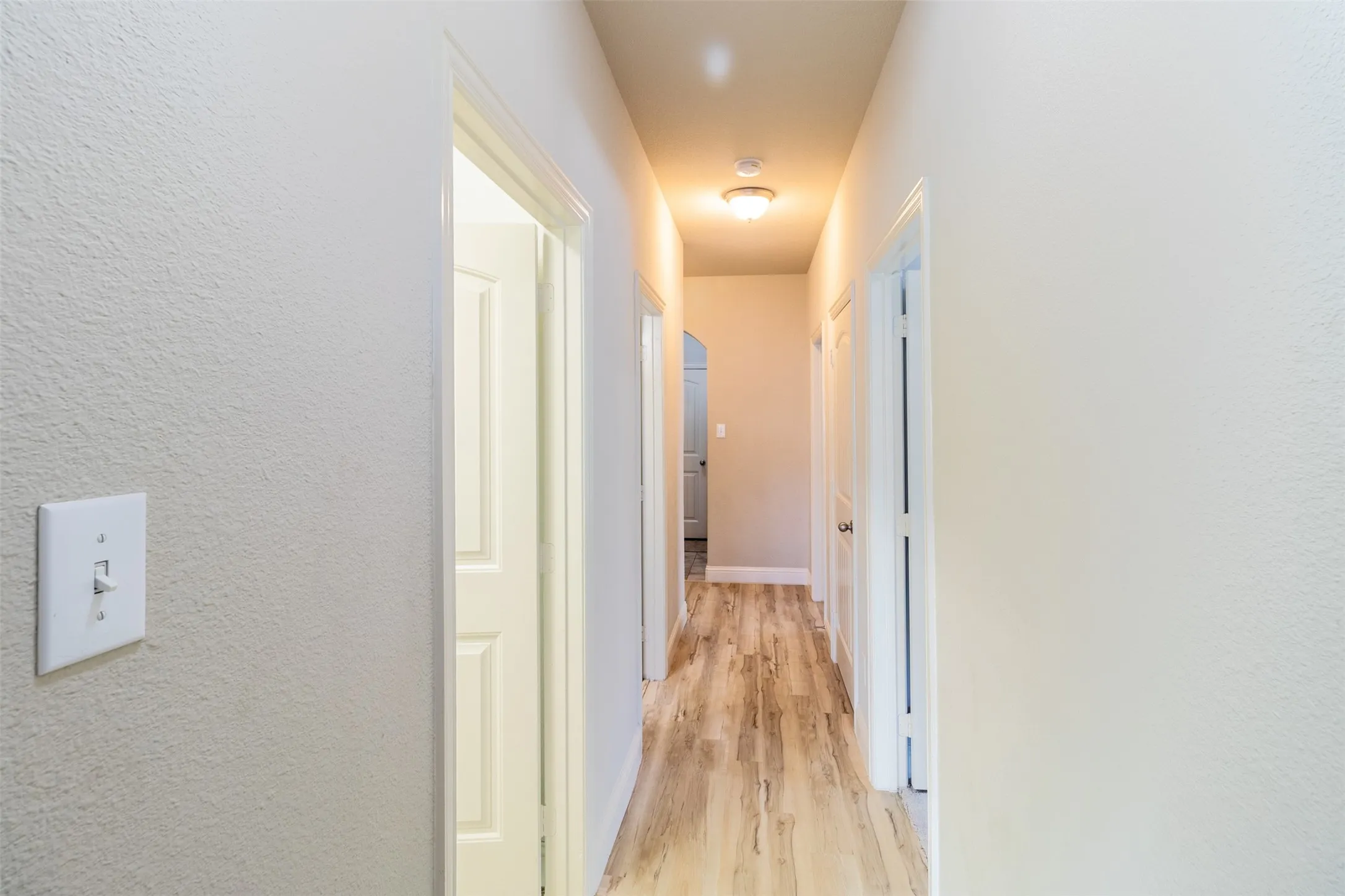 Hallway featuring wood-finish flooring, overhead lighting, and crisp white walls