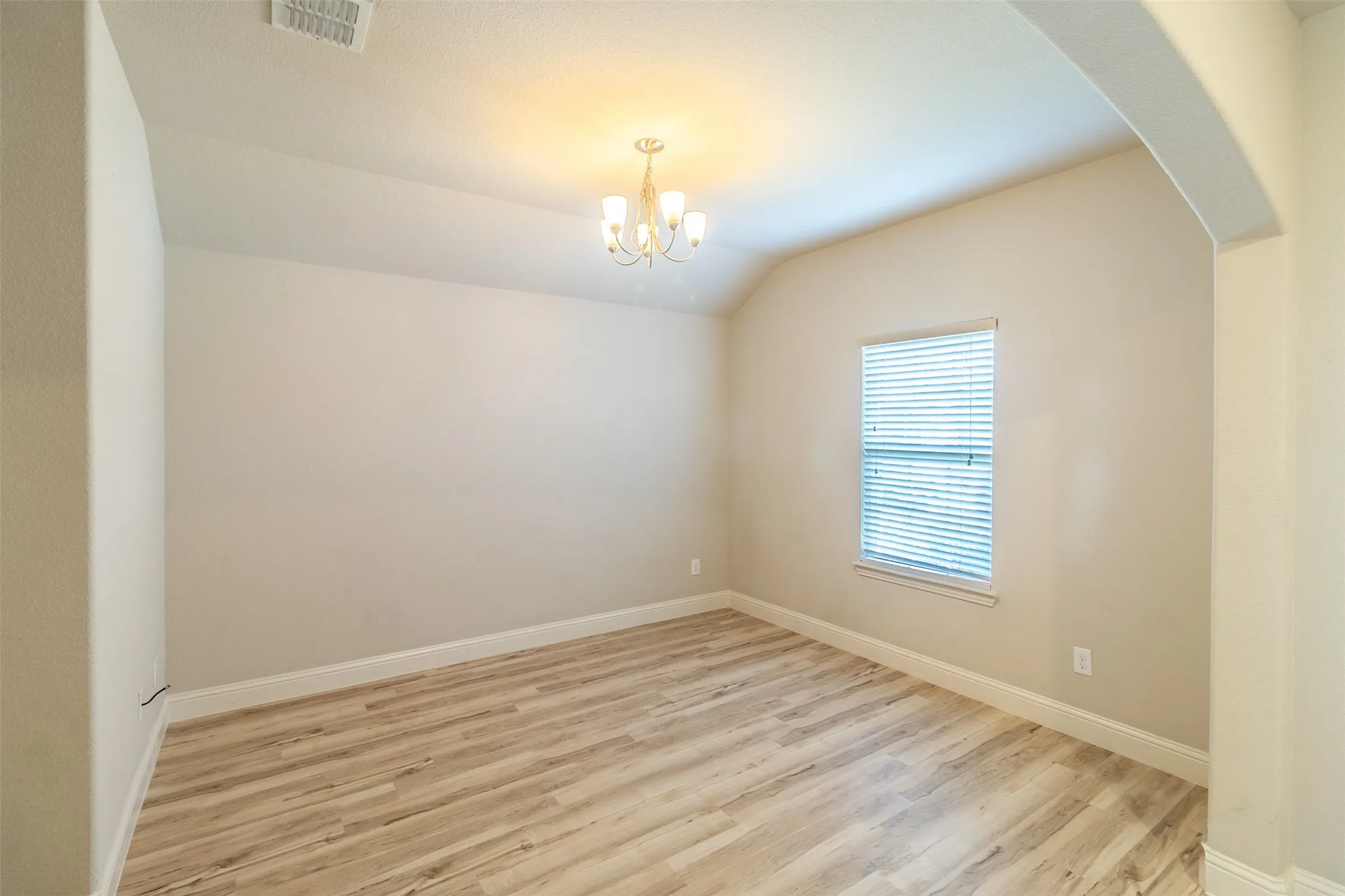 Vaulted ceiling, wood-finish flooring, arched entryway, window with blinds, and a decorative chandelier