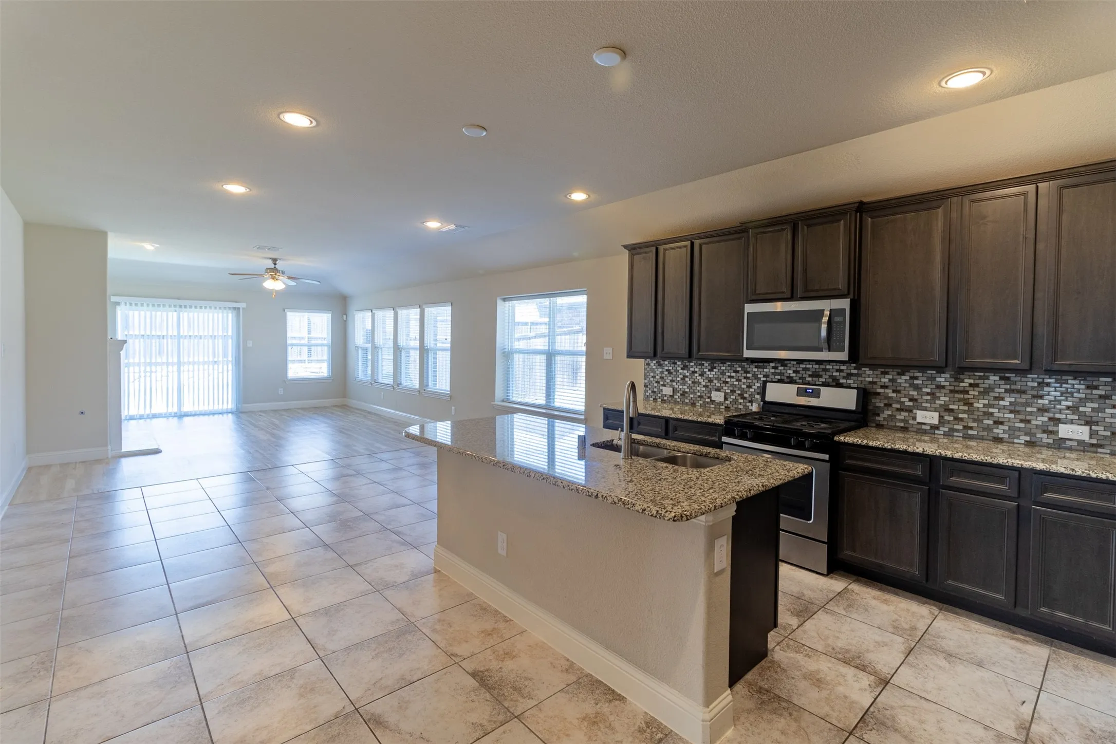 Spacious open-concept layout featuring tile flooring, recessed lighting, dark wood cabinetry, stainless steel appliances, and granite countertops