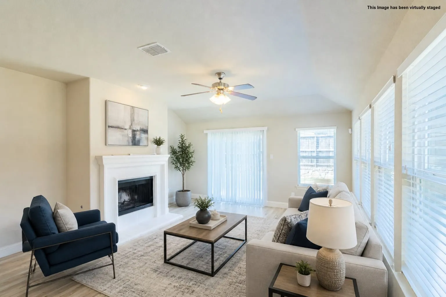 Vaulted ceiling with a ceiling fan, fireplace with a white mantel, sliding glass door, multiple large windows, and wood-finish flooring