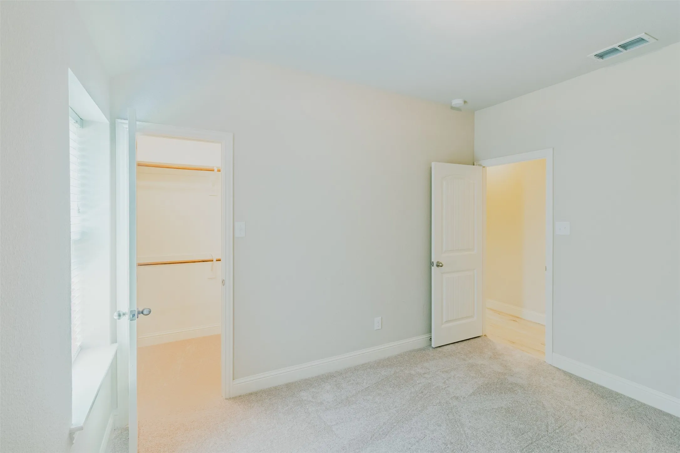 bedroom #2 Room with light gray wall paint, gray carpet, a white framed window with blinds, and a walk-in closet featuring built-in shelving