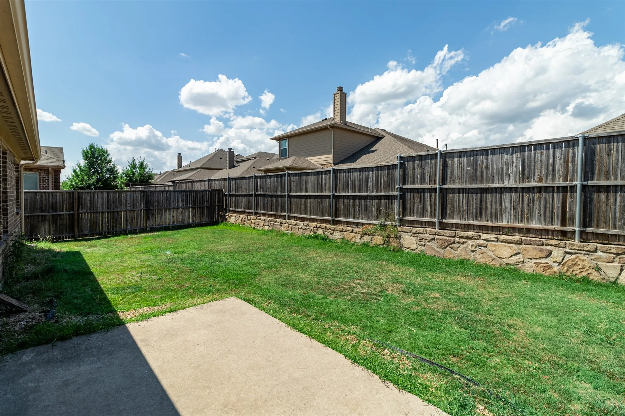Expansive grassy yard featuring a concrete patio, wood privacy fencing, and a stone retaining wall