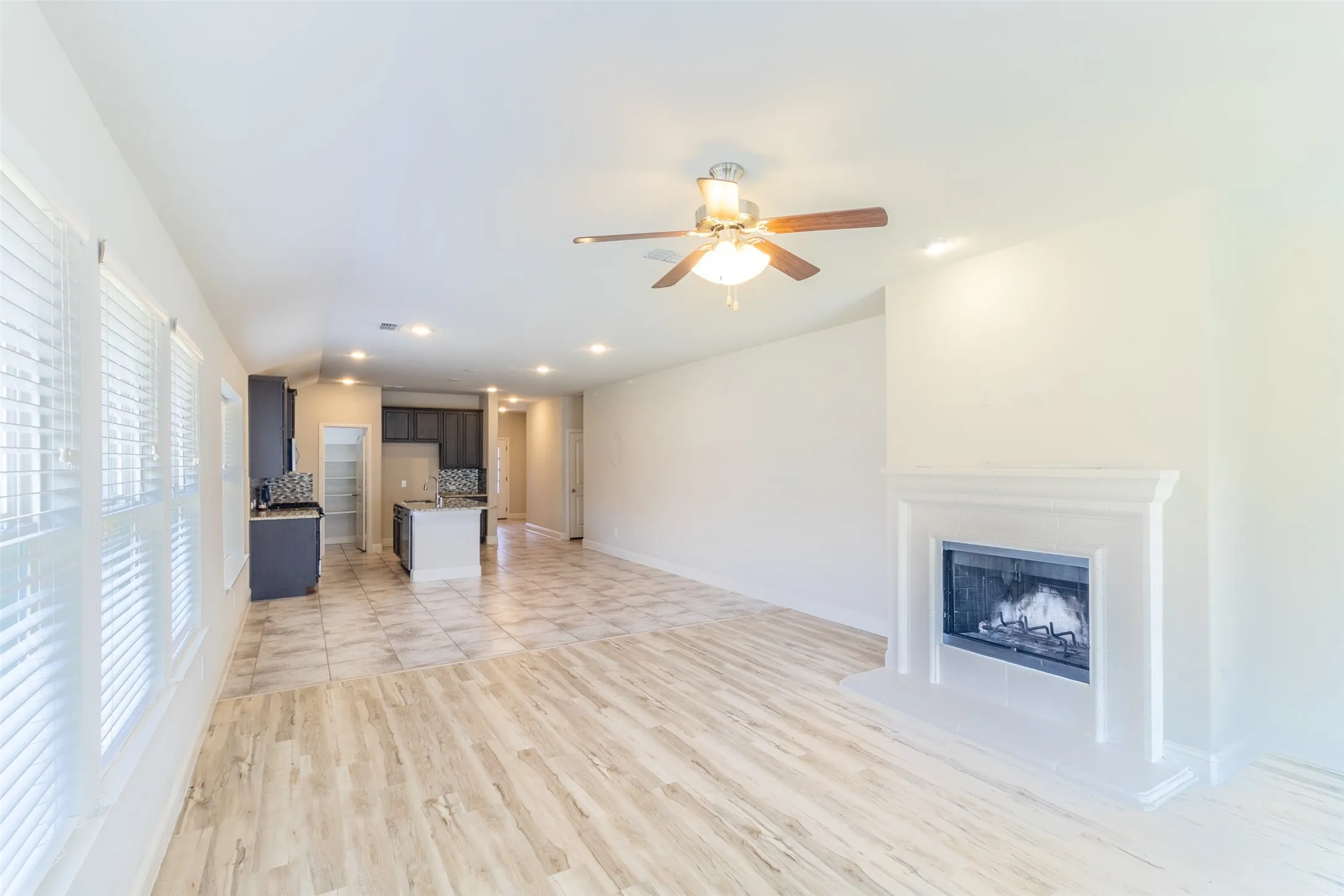 Open-concept living space featuring wood-finish flooring, a traditional fireplace with a mantel, and a ceiling fan
