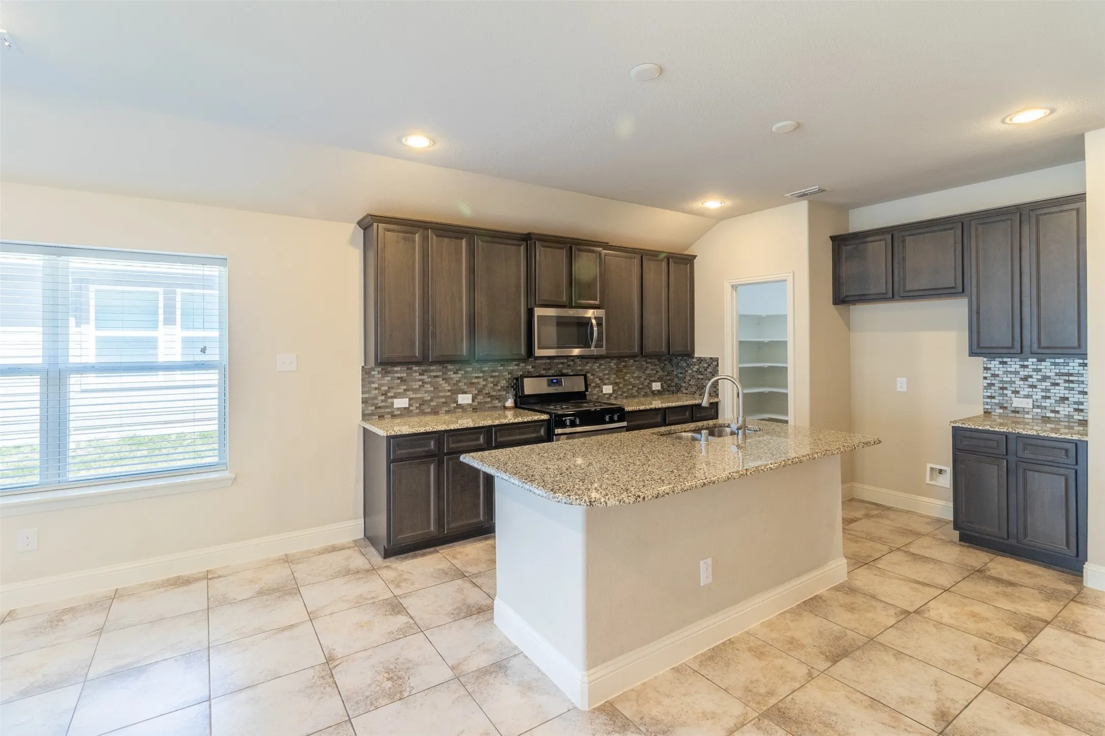 Kitchen featuring a center island with a sink, stainless steel appliances, dark wood-finish cabinetry, and a patterned tile backsplash