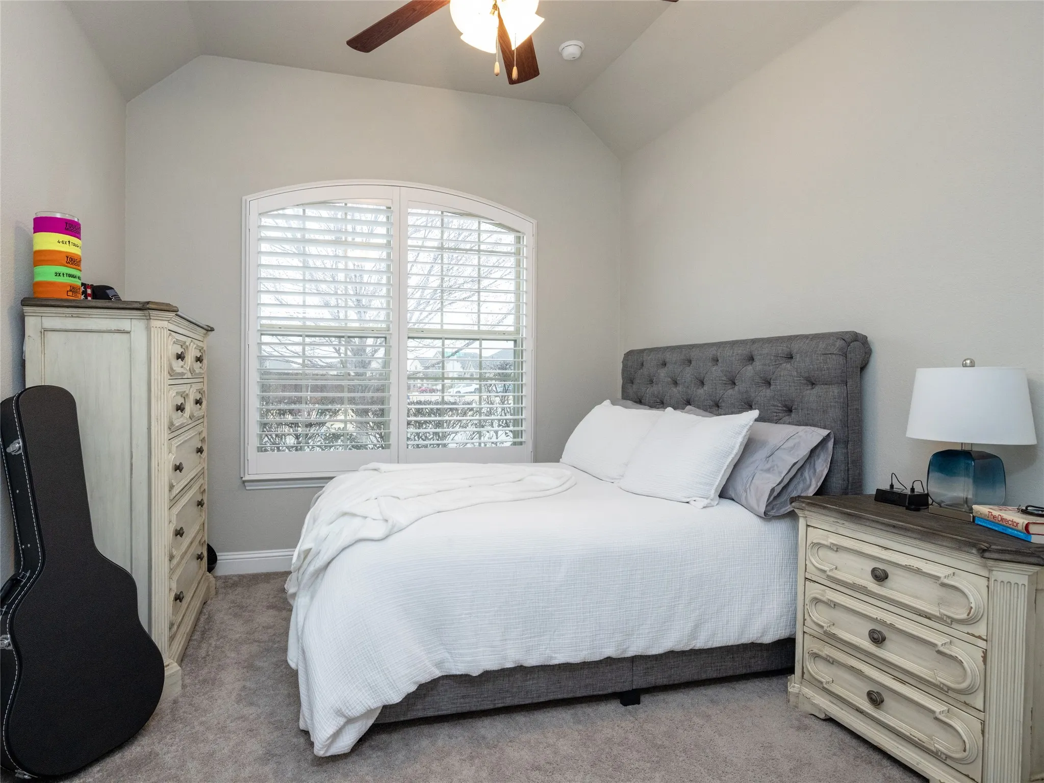 Arched window with plantation shutters, vaulted ceiling, ceiling fan with integrated lighting, and carpet flooring