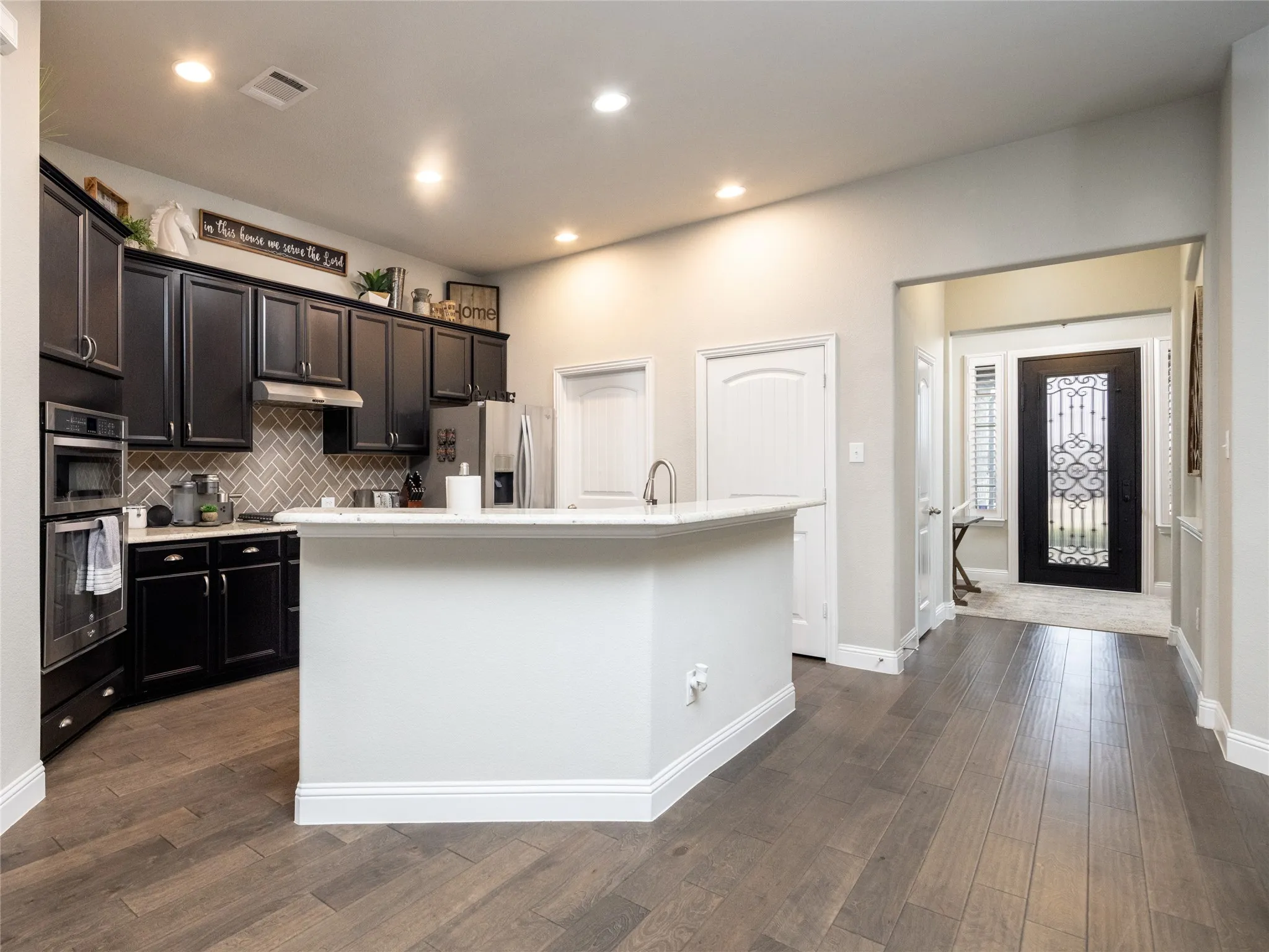 Kitchen featuring dark wood cabinetry, a herringbone tile backsplash, stainless steel appliances, and a central island with a light-toned countertop