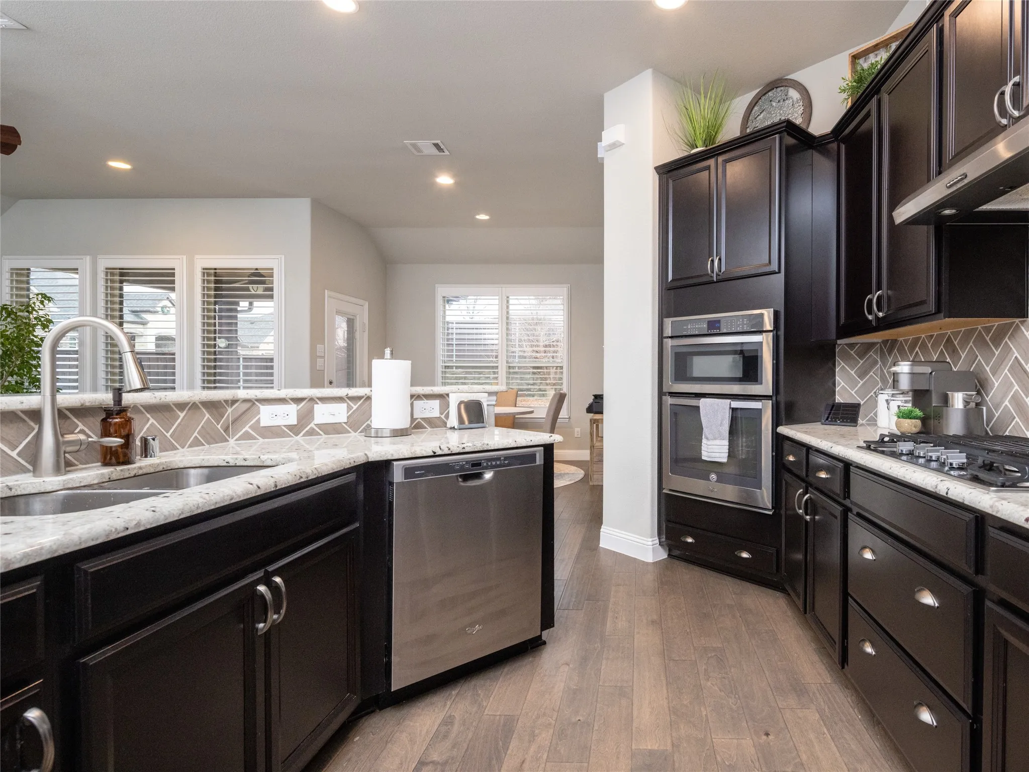 Dark wood-finish cabinetry, stainless steel appliances, granite-style countertops, herringbone tile backsplash, and wood-finish flooring