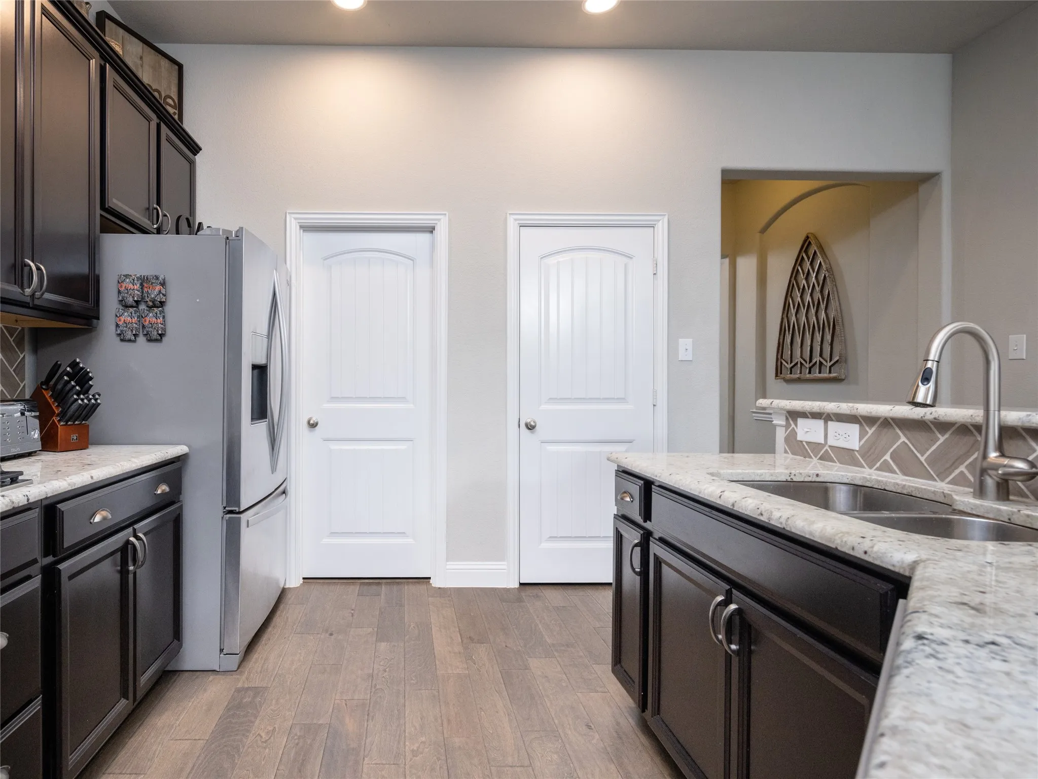 Kitchen featuring dark wood-finish cabinetry, light-toned countertops, a stainless steel sink with a pull-down faucet, wood-finish flooring, and a tiled backsplash