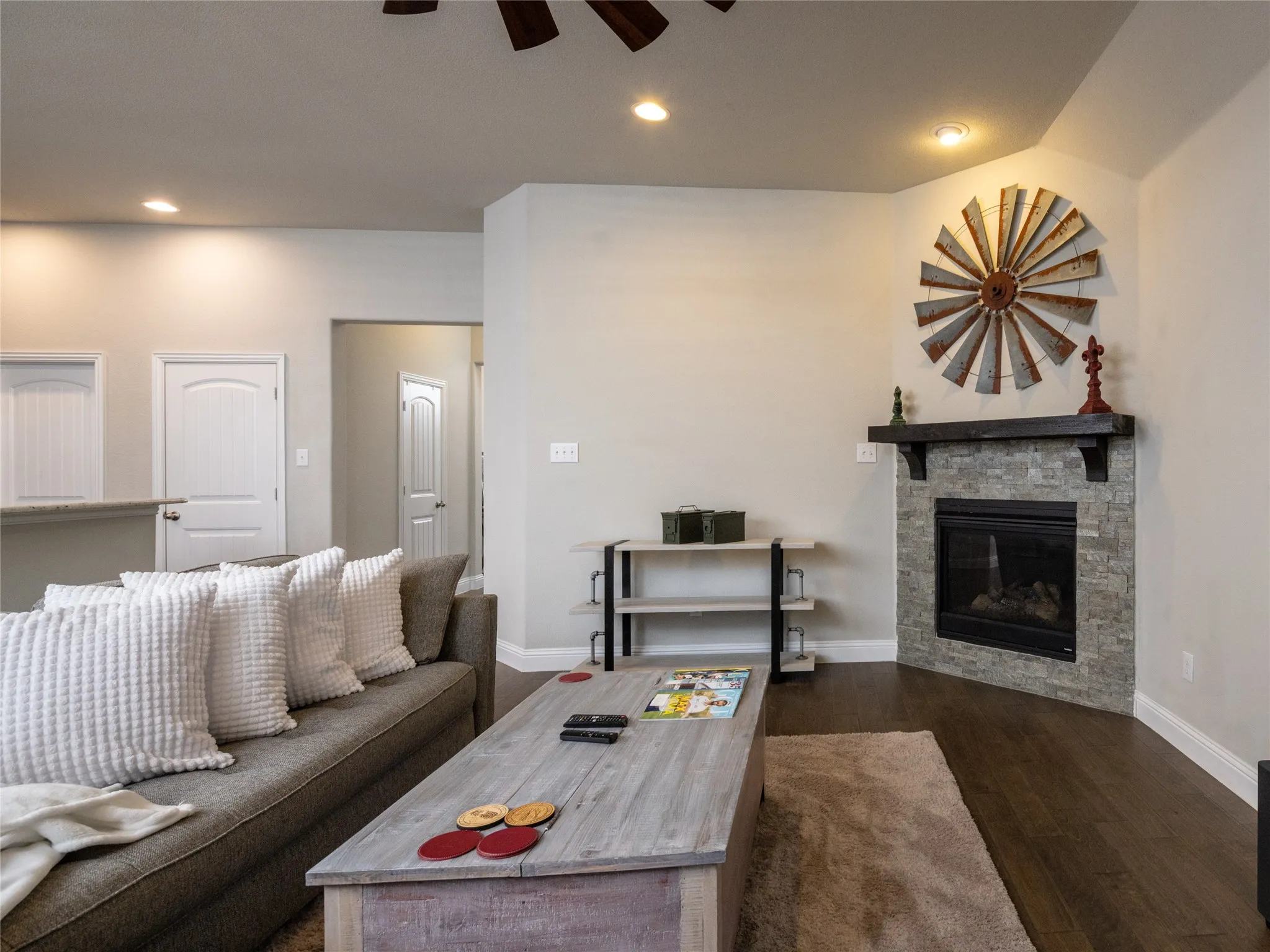 Corner fireplace with stone surround and dark wood mantle, recessed lighting, and wood-finish flooring