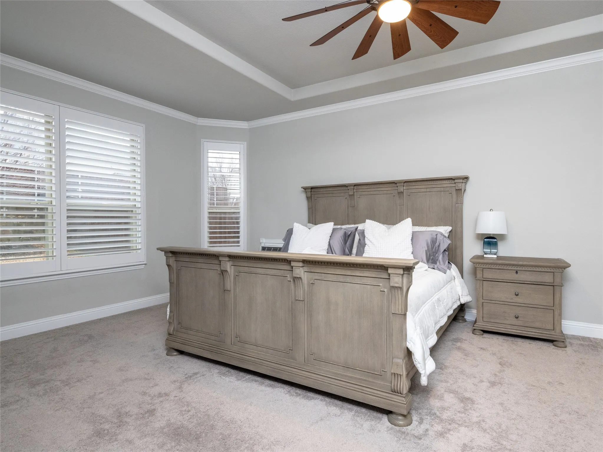 Tray ceiling with crown molding, wood-blade ceiling fan, and light-tone carpeting