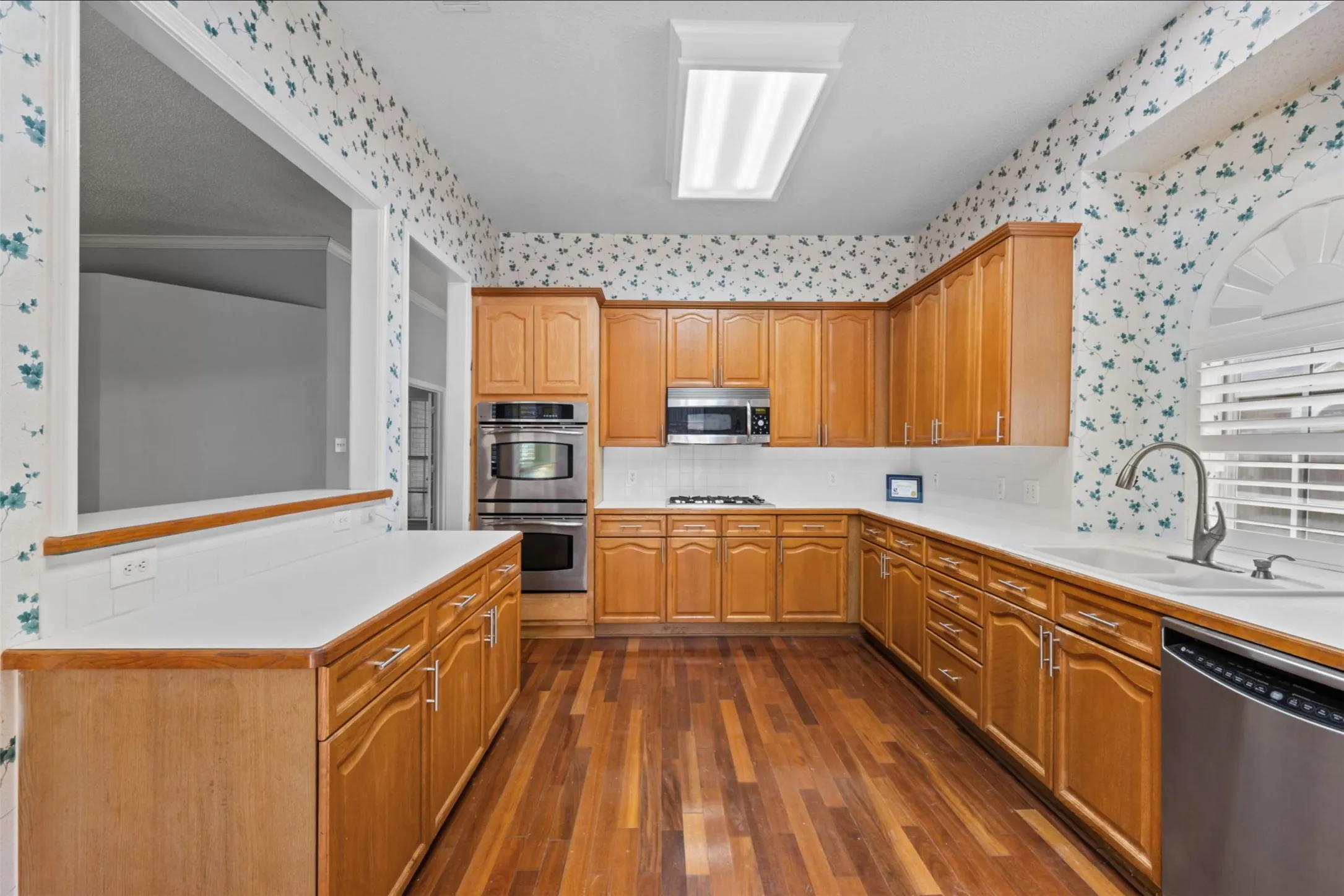U-shaped eat in  kitchen featuring wood cabinetry, stainless steel appliances, solid surface countertops, a built-in double oven, and wood-finish flooring, separate pantry